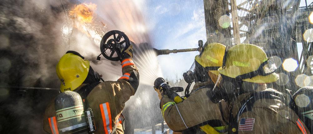三名穿着安全装备的消防员用一根水管灭火.